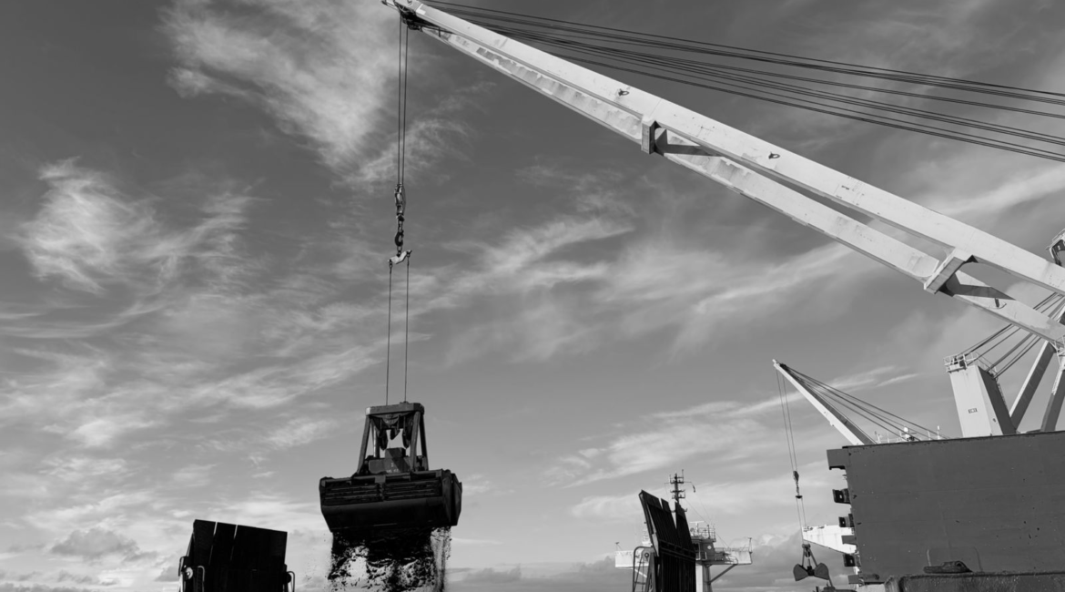 Une benne décharge du vrac d’un navire vers des barges au large