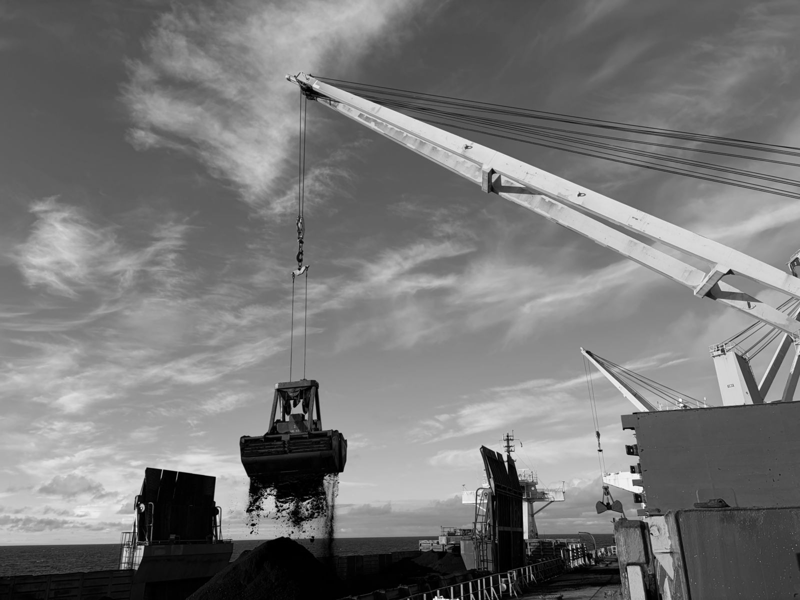 Une benne décharge du vrac d’un navire vers des barges au large